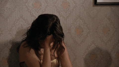 a woman covering her face with her hands in front of a wall with a floral pattern