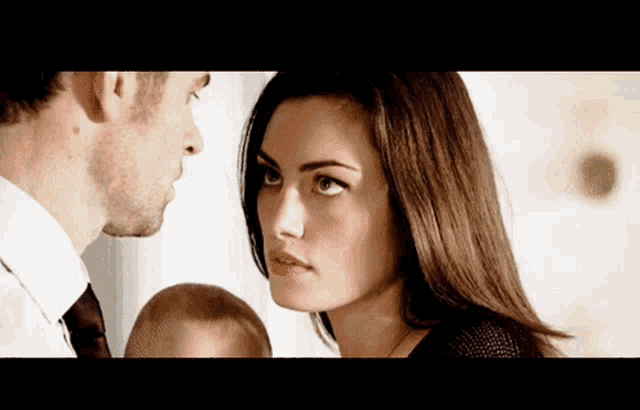 a man and a woman are looking at each other with a baby in the background