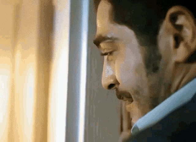 a man with a beard is looking out of a window while wearing a suit and tie .