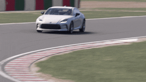 a white car is driving on a track with red and white stripes