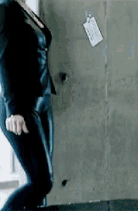 a woman in a black suit is standing in front of a wall with a tag on it .