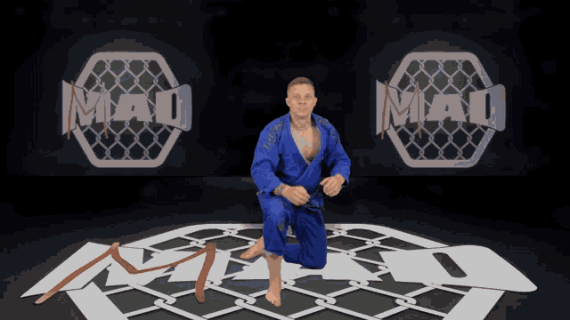 a man in a blue karate uniform is kneeling on a mat in front of a mad logo