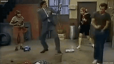 a group of people are dancing in a room while a man is standing on a block .