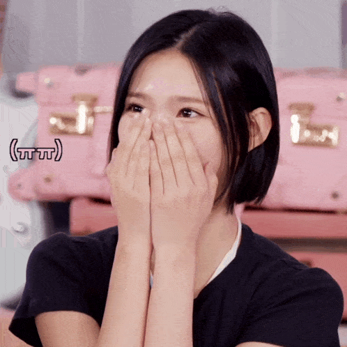 a girl covering her face with her hands and a pink suitcase in the background