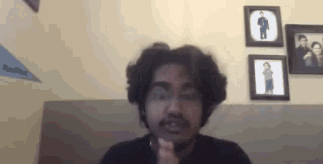 a man with a mustache is sitting in front of a wall with a bunch of pictures on it .