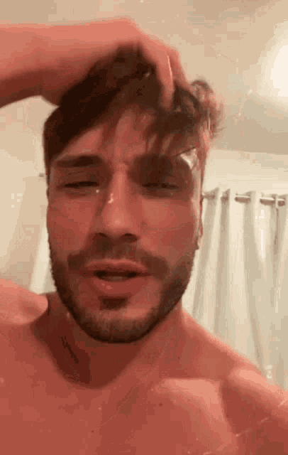 a shirtless man with a beard is washing his hair in a shower .