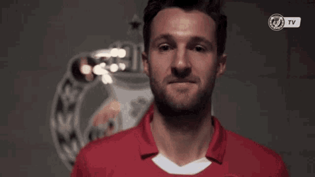 a man in a red shirt is standing in front of a wall with a tv logo on it