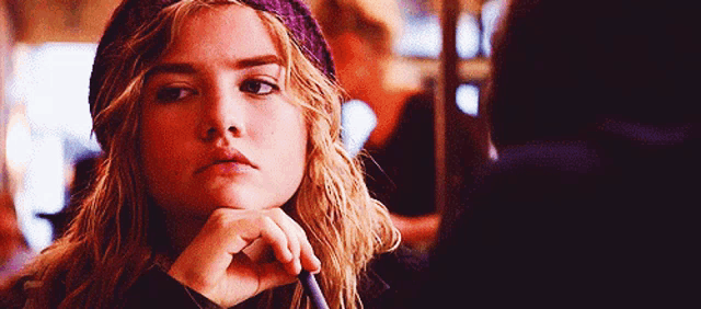 a woman wearing a purple beanie is holding a pen to her chin