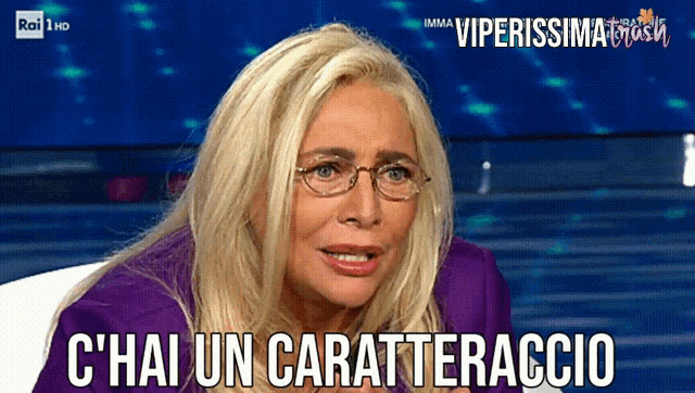 a woman wearing glasses and a purple jacket says c ' hai un carattereraccio