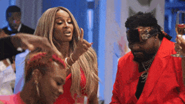 a woman in a red dress is dancing with a man in a red suit holding a glass of champagne .