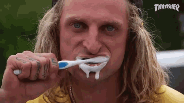 a man is brushing his teeth with a thrasher logo in the background