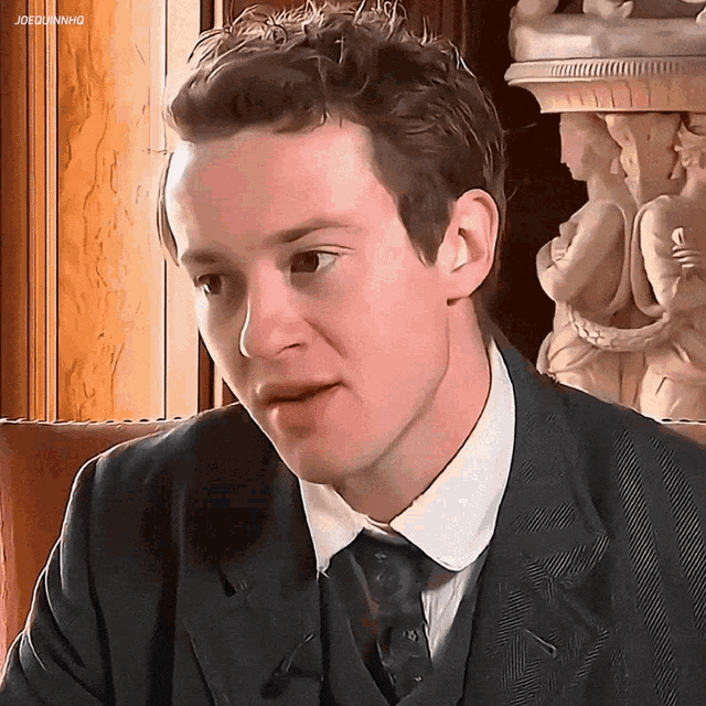 a man in a suit and tie is sitting in front of a statue of a woman with the caption joegunhd