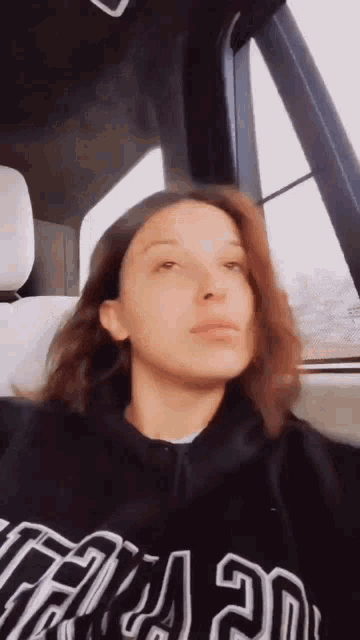 a woman is sitting in the back seat of a car wearing a black hoodie with the word chicago on it .