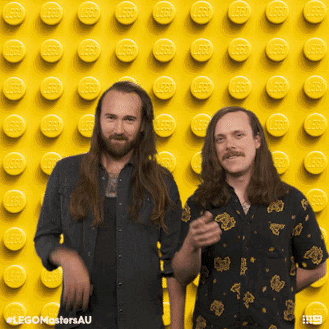 two men standing in front of a lego wall