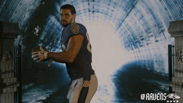 a man in a ravens jersey holds a football in front of a tunnel