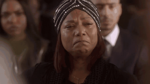 a woman is crying at a funeral while wearing a turban and a black jacket .