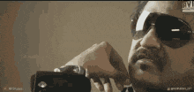 a man wearing sunglasses holds a camera in his hand