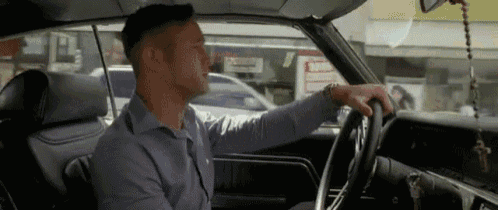 a man is sitting in the driver 's seat of a car and holding the steering wheel .