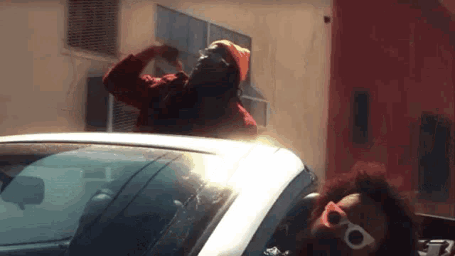 a man in a beanie is standing on top of a white car .