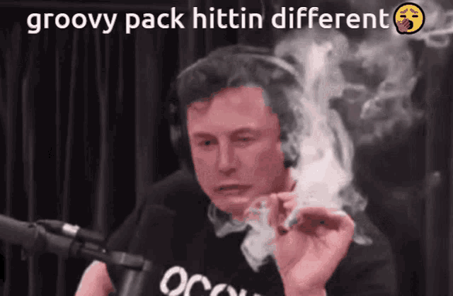 a man smoking a cigarette in front of a microphone with the words groovy pack hittin different below him