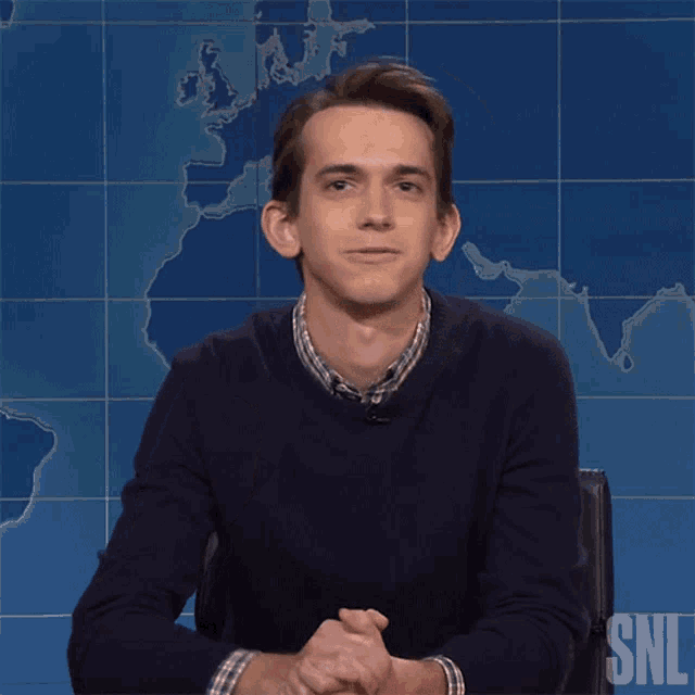 a man sitting in front of a snl sign