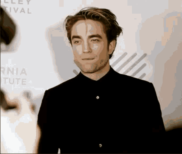 a man in a black shirt is standing on a red carpet talking to someone .