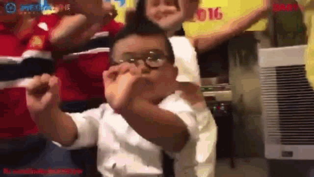 a boy wearing glasses is making a funny face while standing next to a group of people .