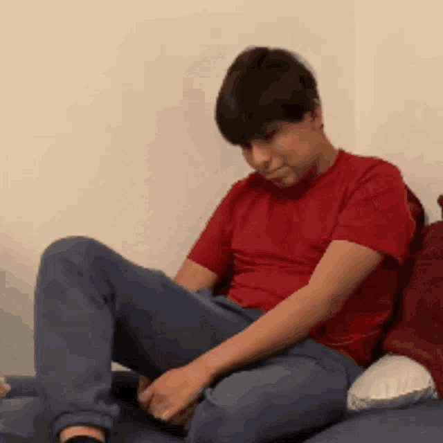 a man in a red shirt sits on a couch with his legs crossed