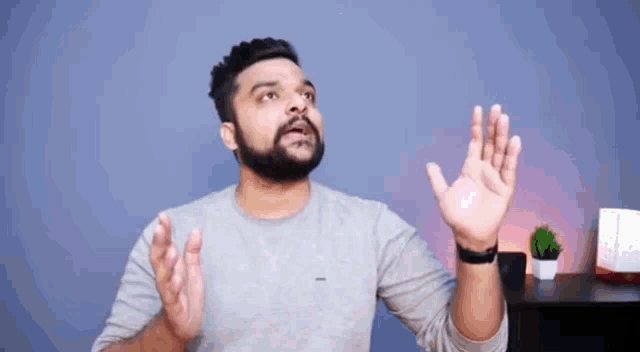 a man with a beard is standing in front of a blue wall making a funny face .