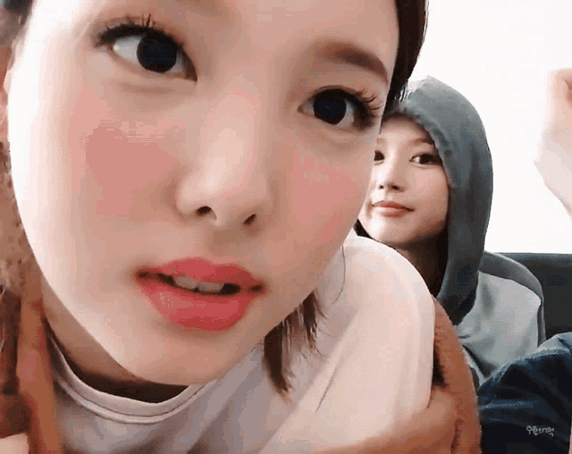 a close up of a woman 's face with a person in the background wearing a hoodie