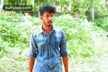 a young man in a denim shirt is standing in the woods .