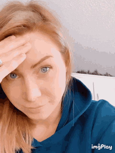 a woman wearing a blue hoodie has her hand on her head