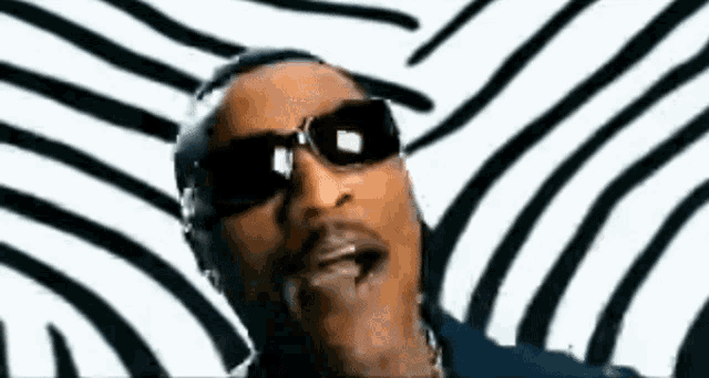 a man wearing sunglasses is standing in front of a black and white striped background .
