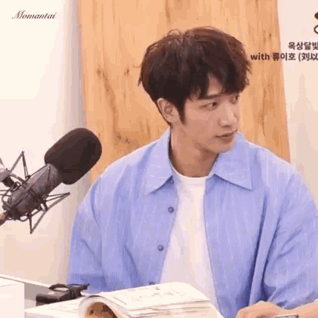 a young man in a blue shirt is sitting in front of a microphone and a book .