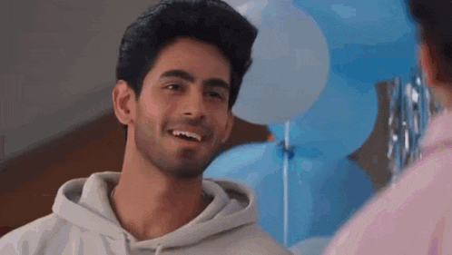 a man in a hoodie is smiling and looking at another man in front of blue balloons .