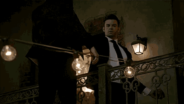 a man in a suit and tie is standing on a balcony looking at a woman