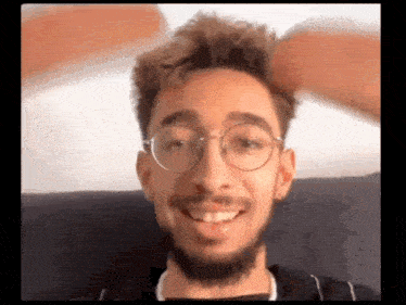 a young man with glasses and a beard is smiling and looking at the camera .