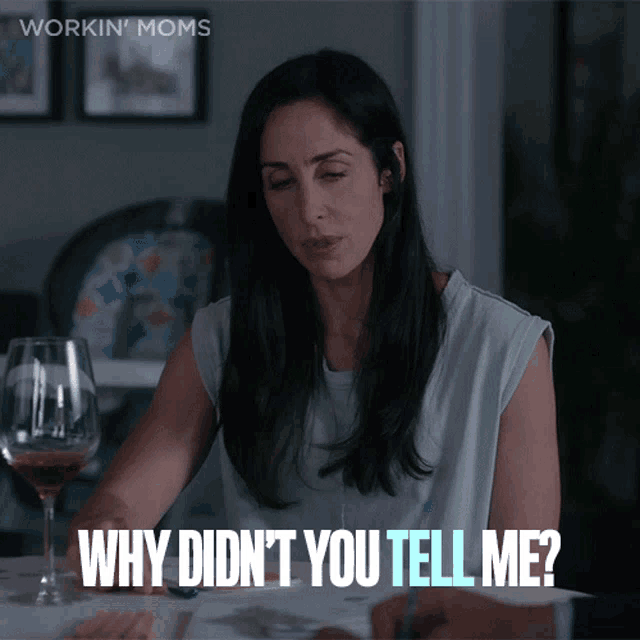 a woman sits at a table with a glass of wine and says " why didn t you tell me "