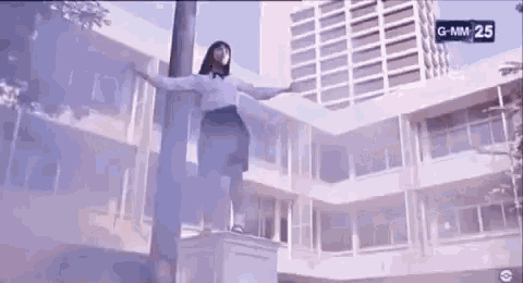 a girl in a school uniform is standing on a ledge in front of a building .
