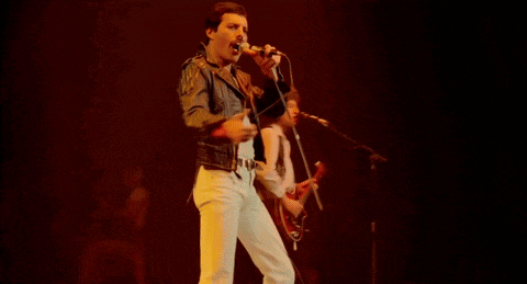 a man with curly hair singing into a microphone in a dark room