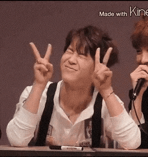 a man is sitting at a table giving a peace sign while another man sings into a microphone .