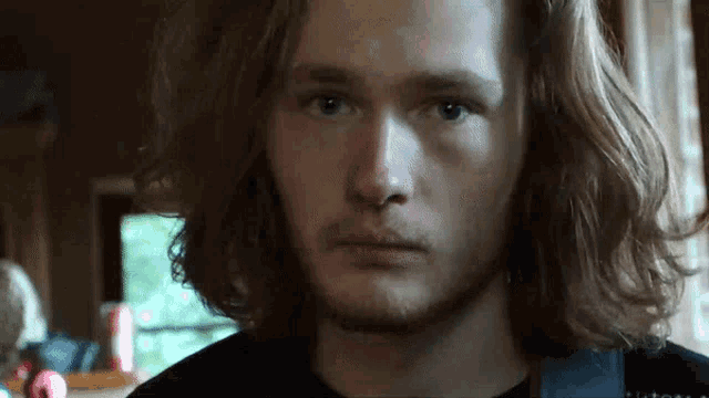 a young man with long red hair and a beard looks at the camera