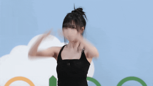 a woman in a black tank top stands with her hands in the air