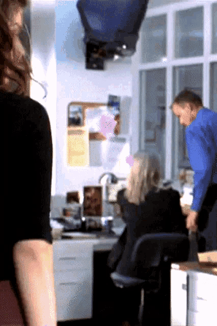a man in a blue shirt stands in front of a woman sitting at a desk