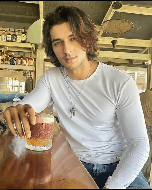 a man in a white shirt sits at a bar with a drink in his hand