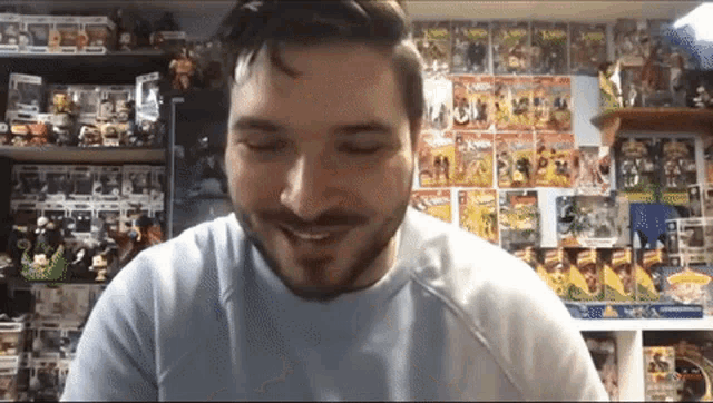 a man with a beard is smiling in front of a wall filled with toys .