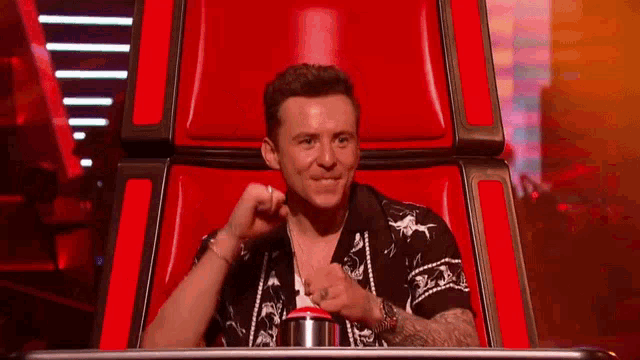 a man is sitting in a red chair with his hand on his face .