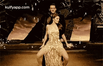 a woman in a gold dress is dancing with a man in a black suit on a stage .