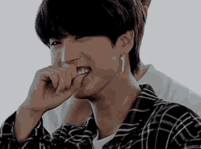 a young man in a plaid shirt is biting his nails and smiling .