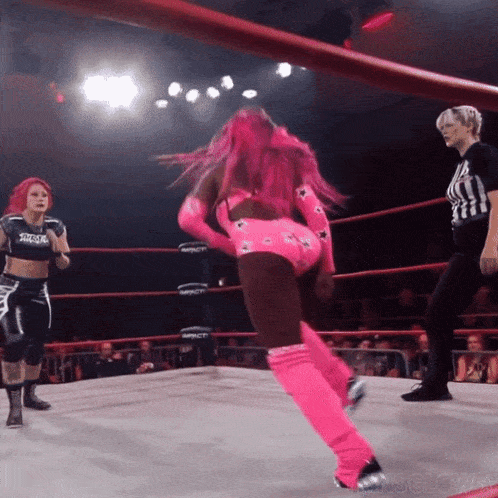 a female wrestler in a pink outfit is standing in a ring with a referee